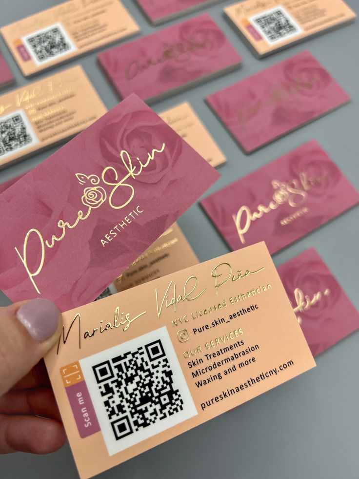 a person holding up a business card in front of some pink and gold business cards