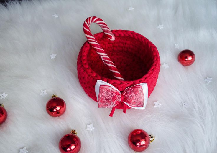 a red basket with a candy cane in it and ornaments around it on a white fur surface