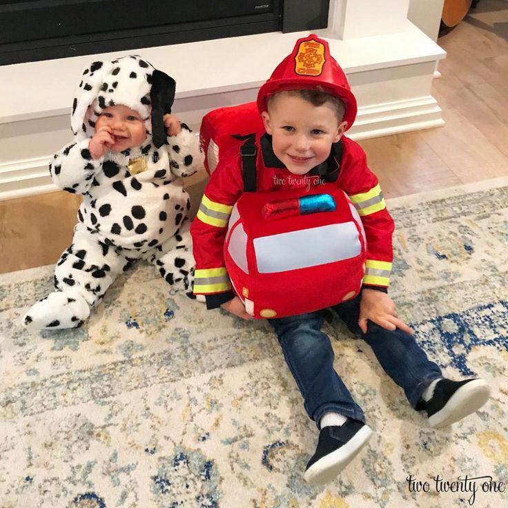 two children dressed in costumes sitting on the floor next to a fireman and dalmatian