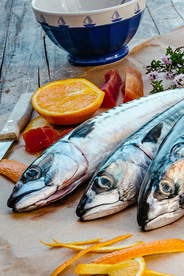 three fish sitting on top of a cutting board next to sliced oranges and other foods