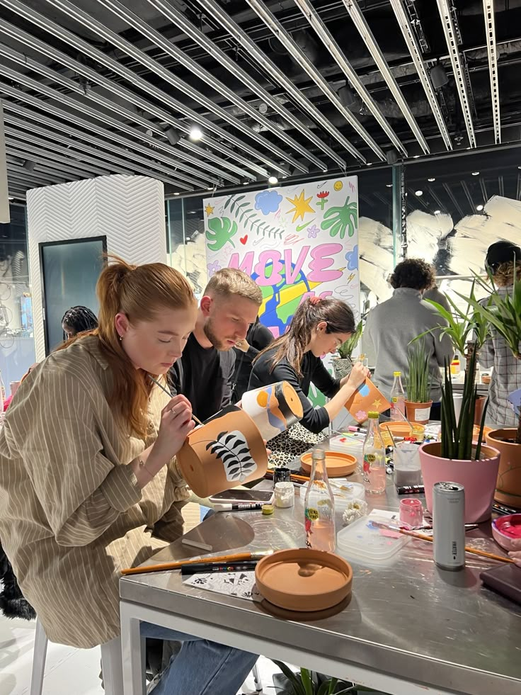 a group of people sitting around a table working on crafting projects with plants in the background