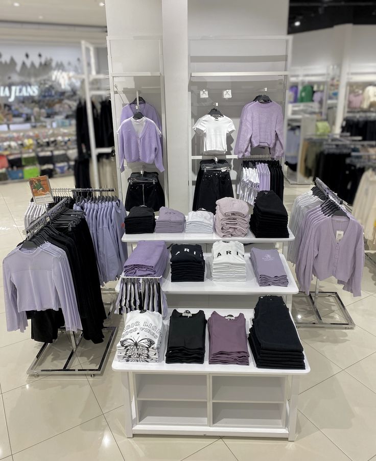 a clothing store display with purple and white shirts on shelves, black and white t - shirts in the background