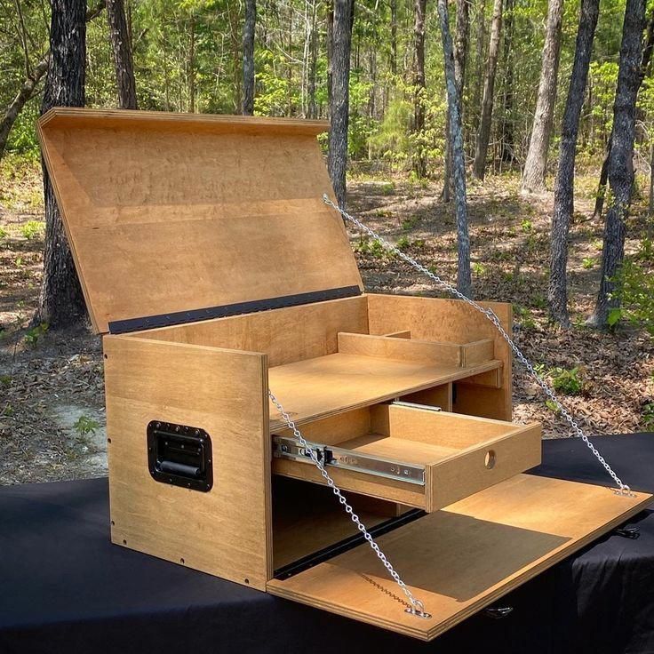 an open wooden box sitting on top of a black table in the middle of a forest