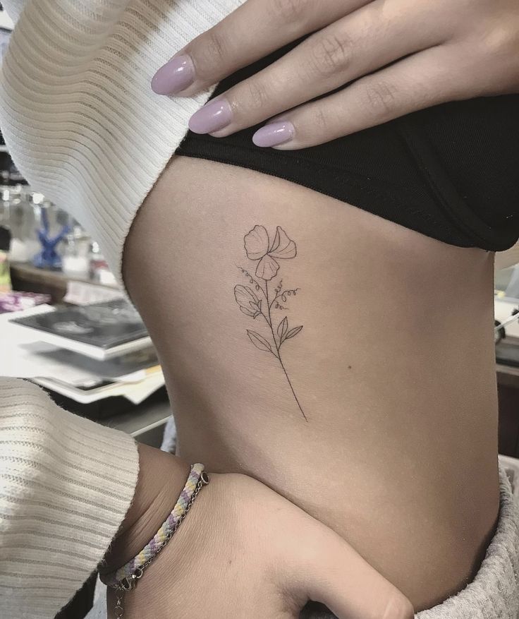 a woman's stomach with a small flower tattoo on her side ribcage