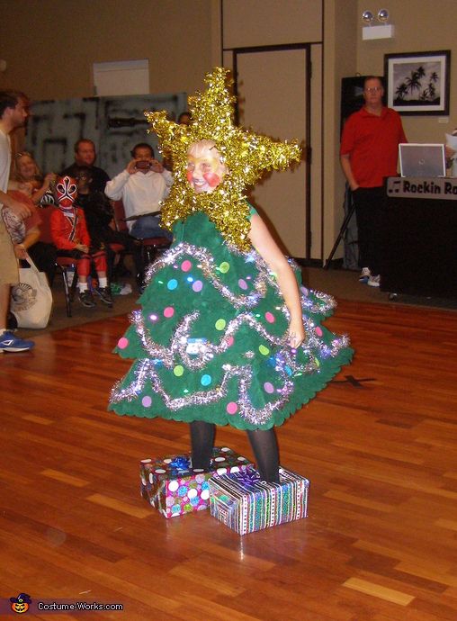 a child in a christmas tree costume standing on top of a box with presents under it