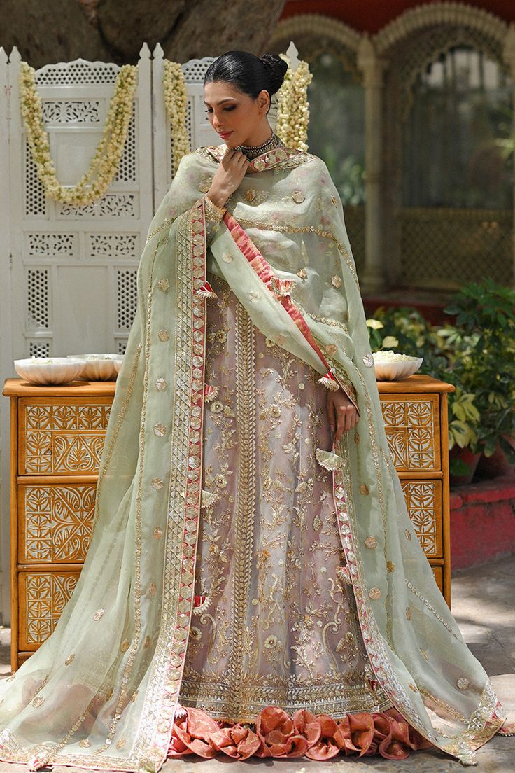 A tulle peshwas, featuring zardoze and resham embroidery, is paired with a salmon pink brocade lehnga and choli. Paired with a mint green organza dupatta accentuated with gota details and tassels.