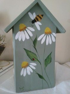 a painted birdhouse with daisies and a bee on it