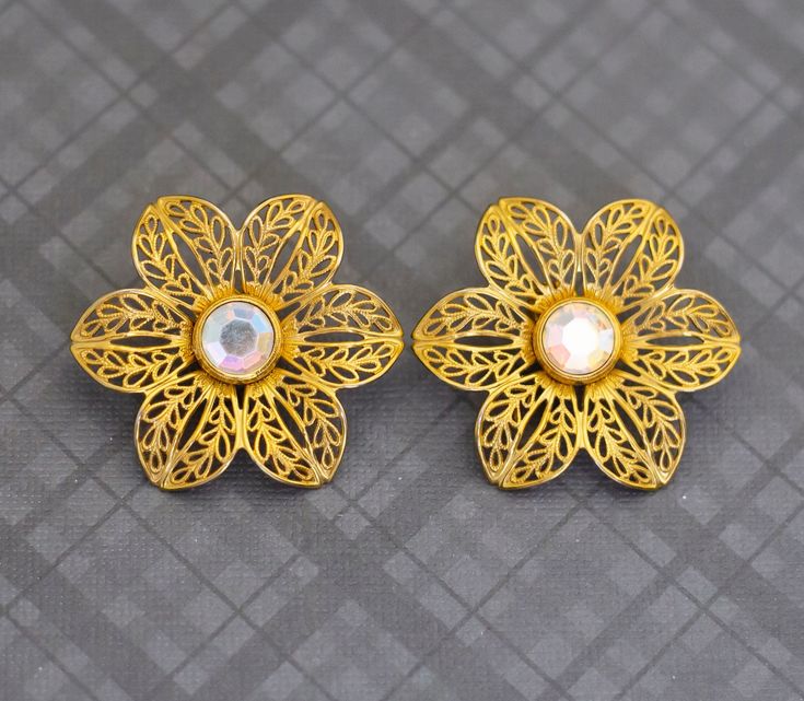 A pair of gold tone flowers stud earrings. There is a beautiful gem at the center.  Made by Avon. GENERAL DESCRIPTION  Vintage Stud Earrings  Color:  Gold tone and clear Brand: Avon Last photo includes measurements of the earrings. If you have any questions please feel free to message me! Vintage Stud Earrings, Flower Earrings Studs, Flower Studs, Earrings Color, Jewelry Earrings Studs, Gold Tones, Etsy Accessories, Jewelry Earrings, Accessory Gift