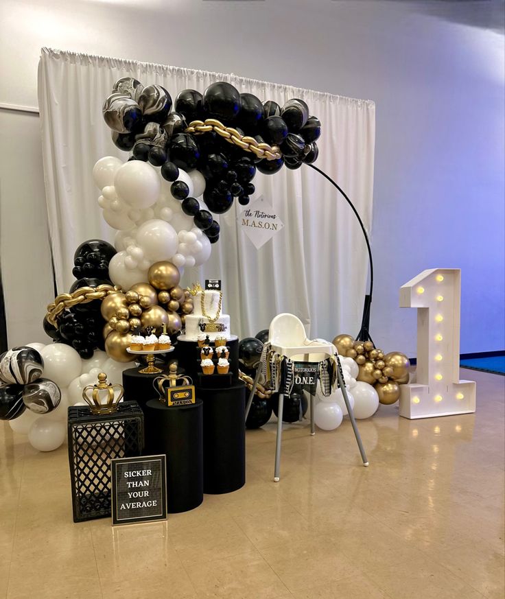 black and gold balloons are on display in front of a white backdrop with the number one