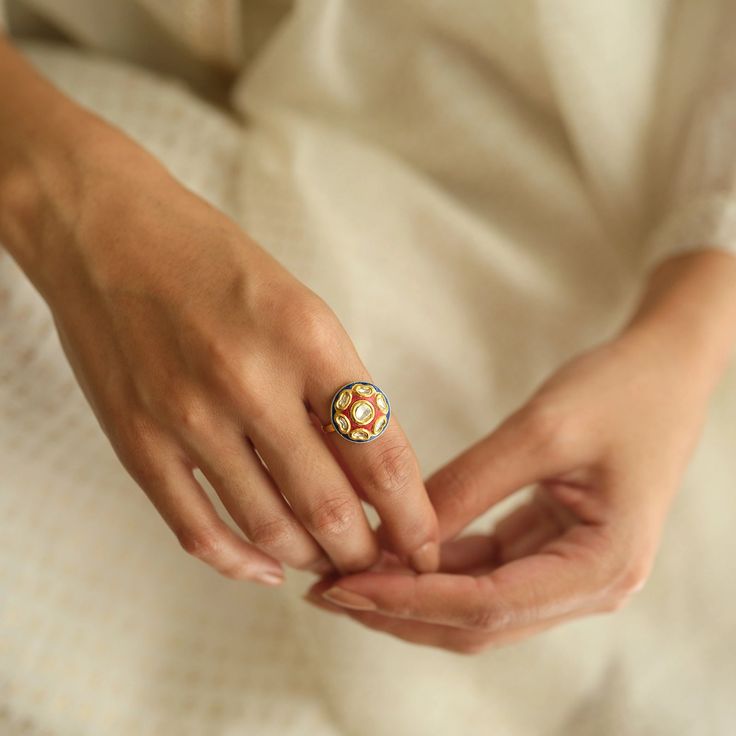 A vibrant melody of the colors, the Benaras Ring paints a vivid picture of India's festive spirit. A rich red Meena (enamel) adorns the disc on which are set polki/uncut diamonds resembling a rosette, a nod to timeless elegance. A border of blue Meena embraces the vivid red, a tribute to the kaleidoscope of colors that adorn India during celebrations.

The Benaras Ring, in its vivid simplicity, carries the heart of a culture's joyful vibrancy. Traditional Yellow Gold Ruby Ring For Wedding, Traditional Yellow Gold Ruby Wedding Ring, Yellow Gold Meenakari Rings As Gift, Yellow Gold Meenakari Ring For Gift, Traditional 22k Gold Ruby Ring, Traditional 22k Gold Ruby Ring For Wedding, Traditional Ruby Ring In Yellow Gold, Traditional 22k Gold Wedding Ring, Traditional Multi-stone Oval Rings