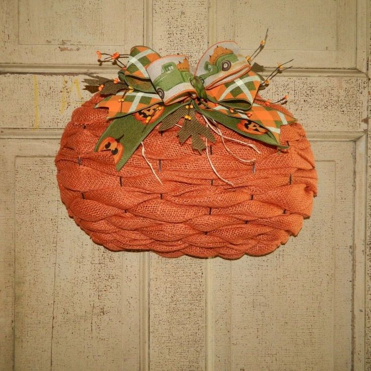 an orange pumpkin shaped wreath hanging on a door with green and orange ribbon around it