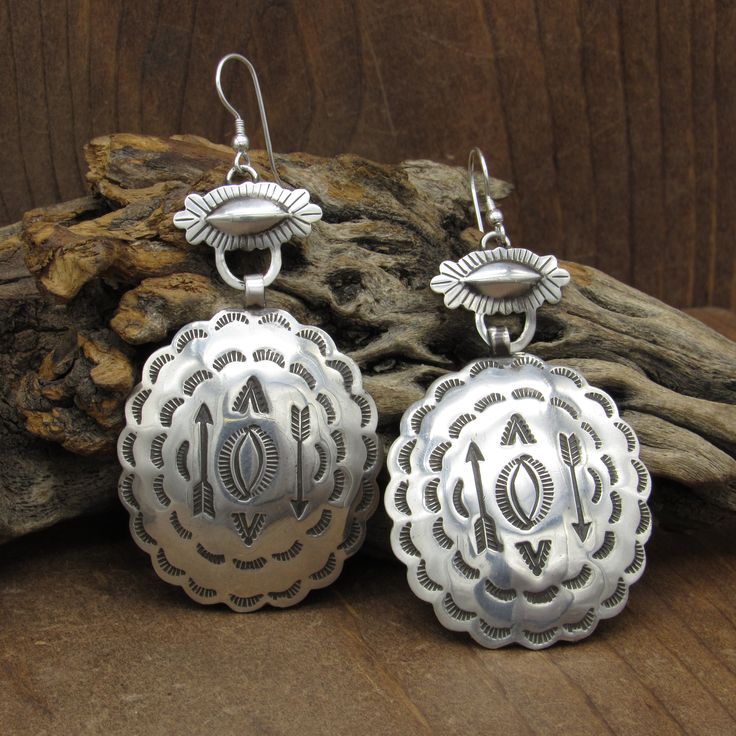 "Sterling silver Southwestern dangle wire earrings. The top of the earrings is 11/16\" tall x 13/16\" wide. The oval concho which hangs below is 1 3/4\" tall x 1 1/2\" wide. There are arrows and other stamp work on the conchos. The edge is scalloped. A sterling silver ear wire finishes the earrings. There is no hallmark on the earrings. We tested the metal and verified it is sterling silver. The earrings are in good condition. Thank you for looking. Please let us know if you have questions. ERNG Western Style Dangle Earrings For Pierced Ears, Oval Southwestern Sterling Silver Earrings, Western Style Teardrop Silver Jewelry, Western Style Silver Teardrop Jewelry, Southwestern Silver Concho Earrings, Silver Southwestern Round Earrings, Silver Western Style Dangle Jewelry, Western Style Silver Dangle Jewelry, Artisan Concho Dangle Jewelry