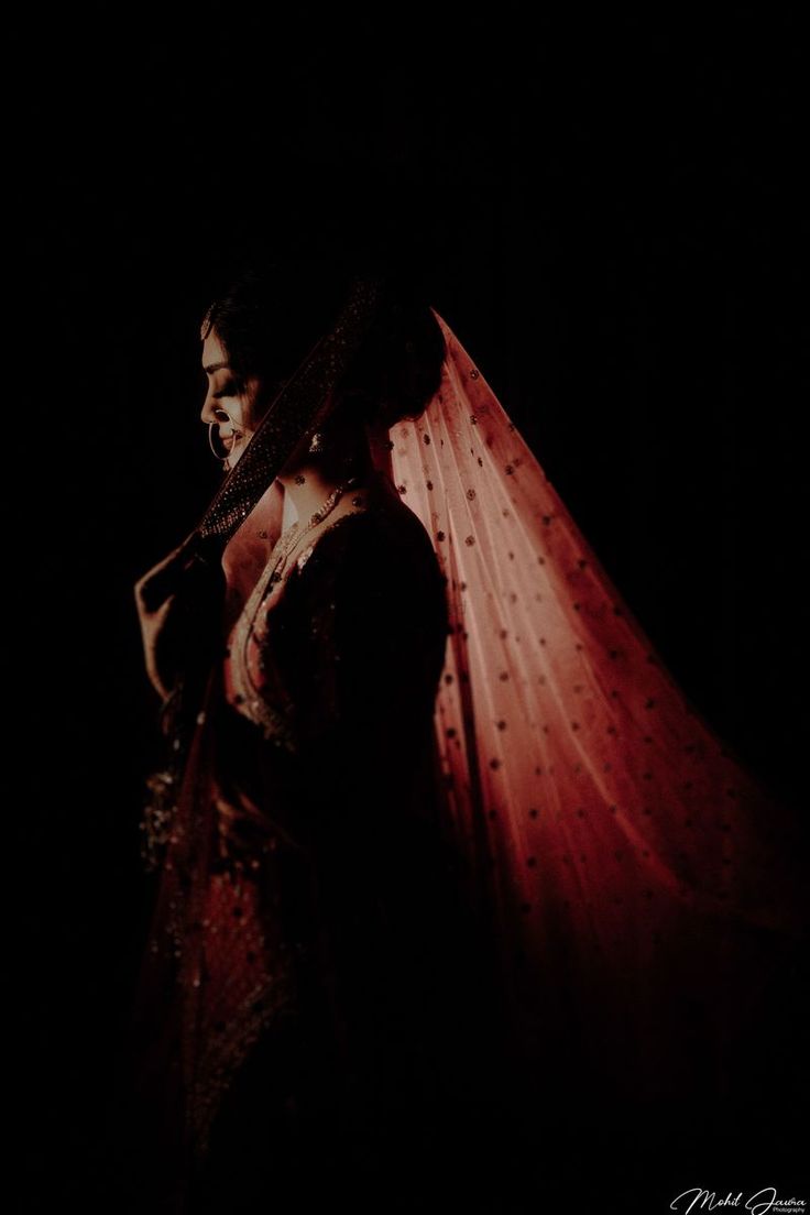 a woman standing in the dark wearing a red veil