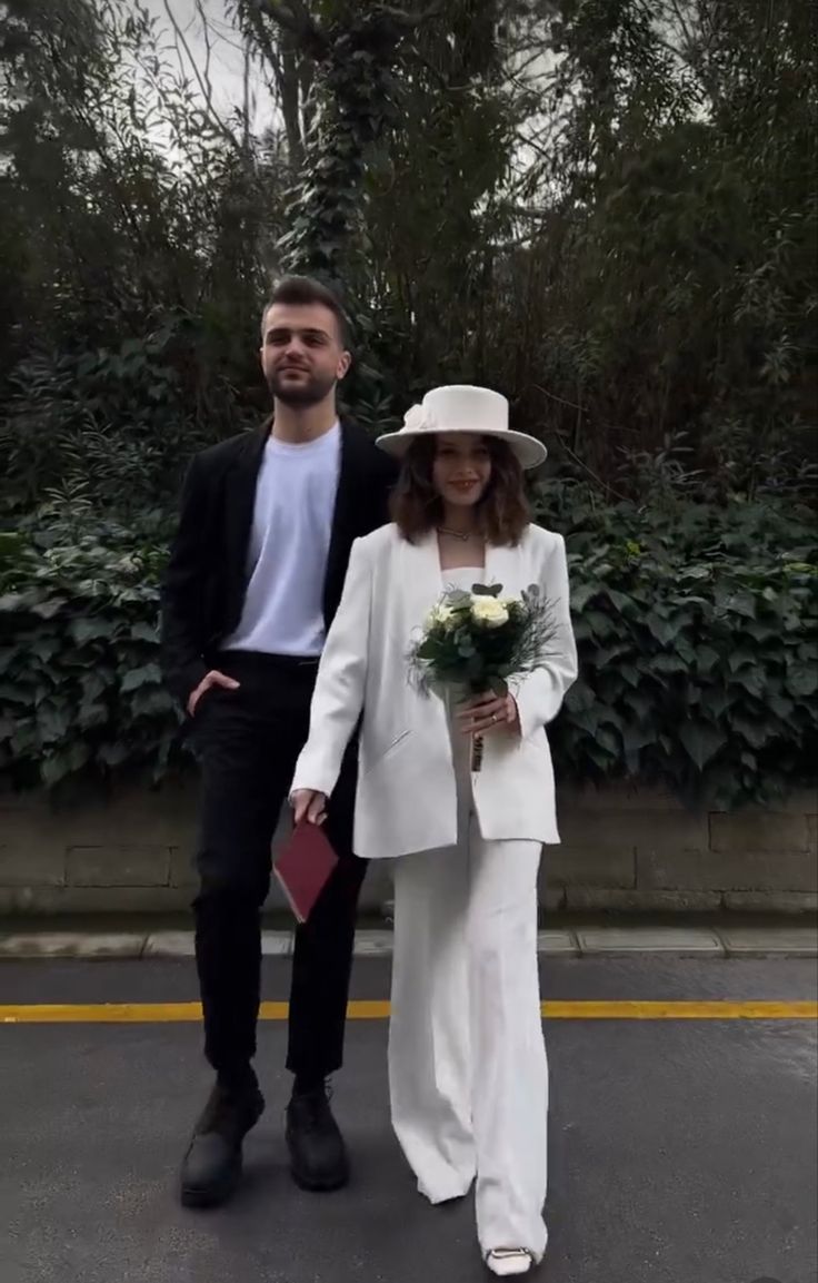 a man and woman walking down the street holding flowers in their hands while wearing white outfits