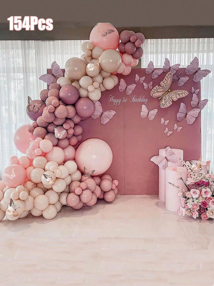 the balloon arch is decorated with pink and white balloons, butterflies, and streamers