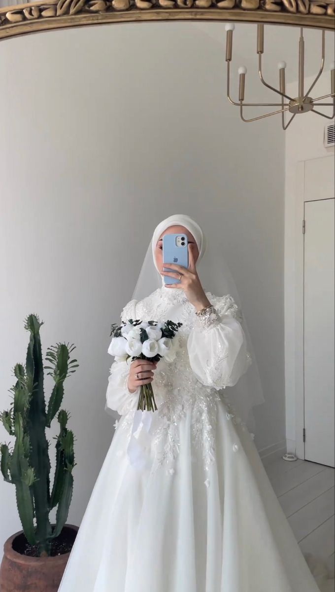 a woman in a white wedding dress taking a selfie with her cell phone while holding a bouquet of flowers