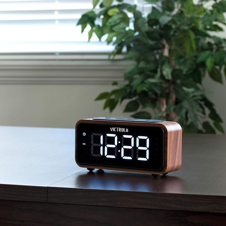 an alarm clock sitting on top of a wooden table next to a potted plant