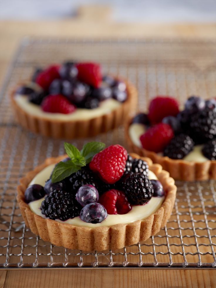 three tarts with berries and blueberries are sitting on a cooling rack, ready to be eaten