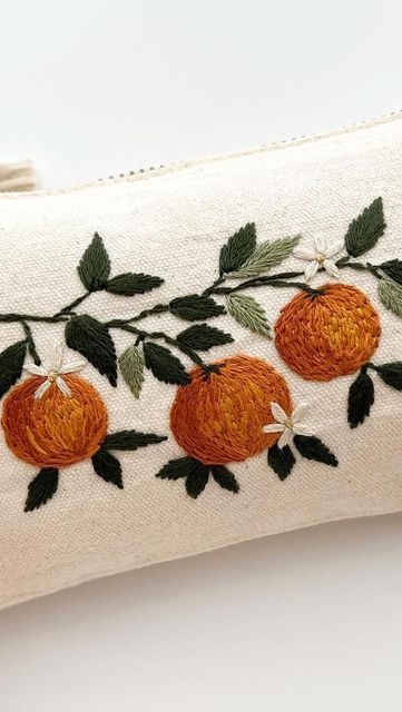 an embroidered pillow with oranges and leaves on it's side, sitting on a white surface