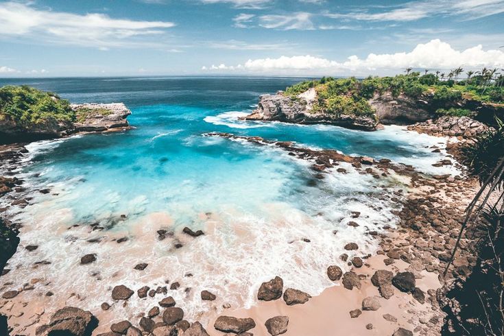 an aerial view of the ocean with rocks and blue water in the foreground, surrounded by lush green trees