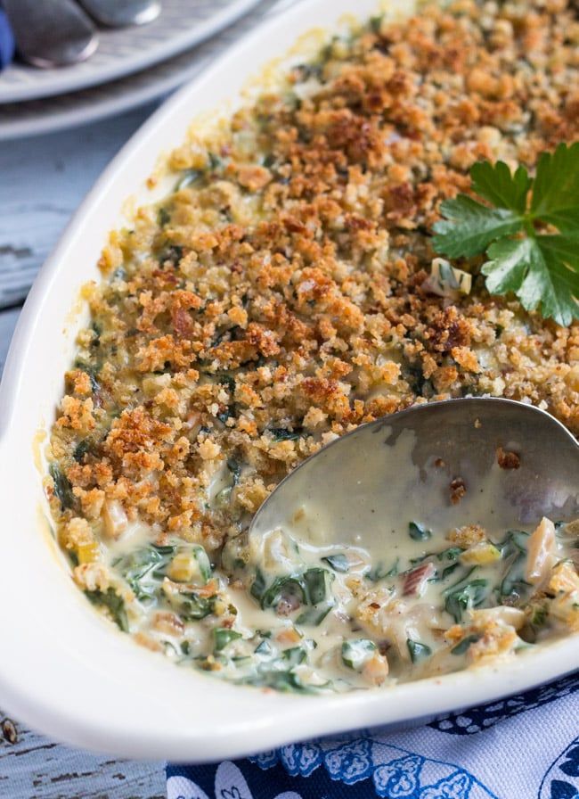 a spoon is in a casserole dish with spinach and bread crumbs