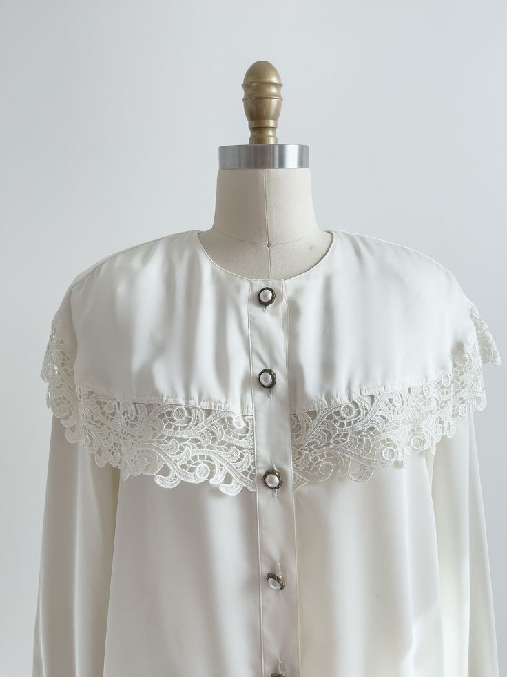 A lovely cream blouse, with a dramatic cape collar trimmed in lace, and ornate buttons down the front. ☛   m e a s u r e m e n t s   ☚ Best for: M Bust: 40 Waist: 40 Shoulders: 16 Length: 25 ☛   d e t a i l s   ☚ Era: 1980s Material: polyester Condition: very good; the buttons are tarnished. ☛   v i s i t   t h e   s h o p   ☚ https://etsy.me/2Nd23kg ☛   instagram ┇ poppycockvintage ☛   facebook ┇ poppycockvintage Vintage Fashion Lace Collar Long Sleeve Blouse, Vintage Fashion Long Sleeve Blouse With Lace Collar, Vintage Long Sleeve Blouse With Lace Collar, Vintage Blouse With Lace Cuffs And Collar, Vintage White Long Sleeve Top With Lace Trim, Vintage Tops With Lace Cuffs And Peter Pan Collar, Vintage Top With Peter Pan Collar And Lace Cuffs, Vintage Lace Collar Button-up Top, Cottagecore Long Sleeve Top With Lace Collar