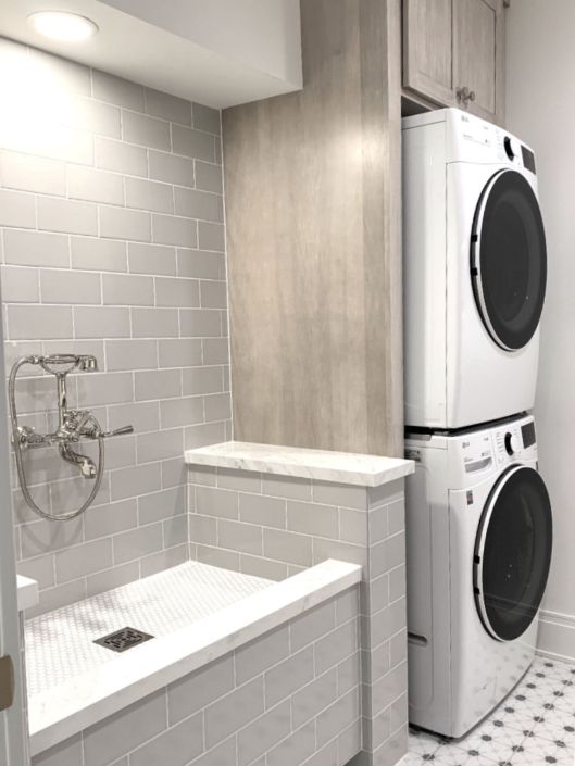 a washer and dryer in a bathroom with white tiled walls, flooring and cabinets