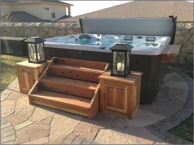 a hot tub sitting on top of a stone patio next to a wooden table and steps