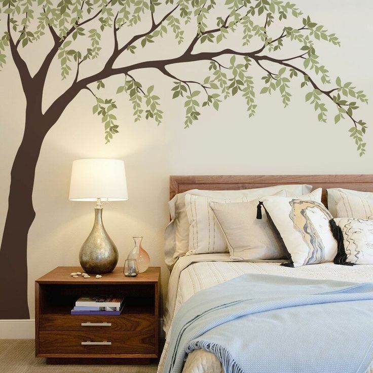 a bedroom with a tree painted on the wall next to a night stand and nightstand