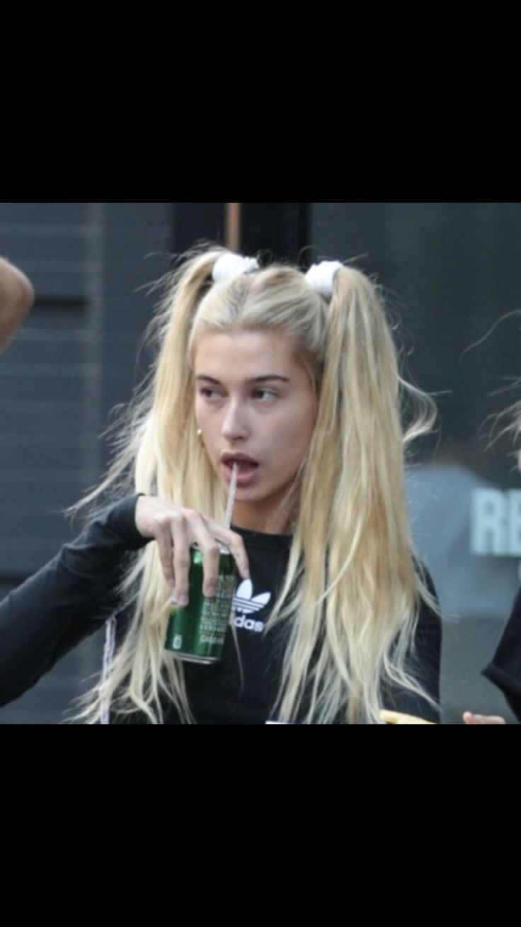 a woman with long blonde hair holding a green drink in her hand and pointing to the side