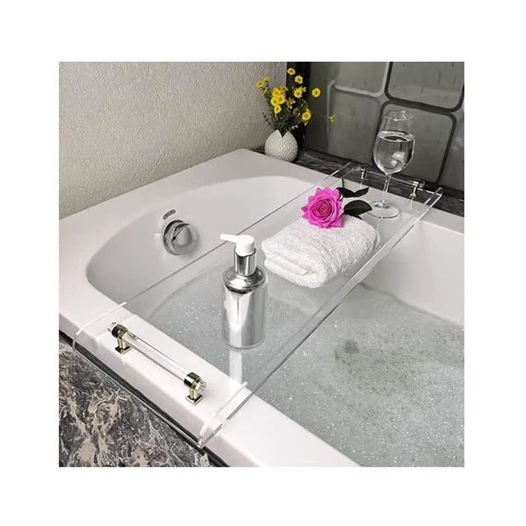 a white bath tub sitting next to a glass vase filled with flowers and wine glasses