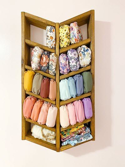 an open wooden shelf filled with lots of cloths on top of a white wall