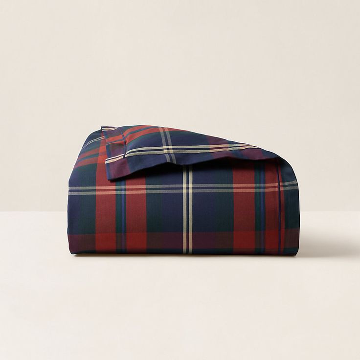 a red and blue plaid sheet set on top of a white table with a pillow