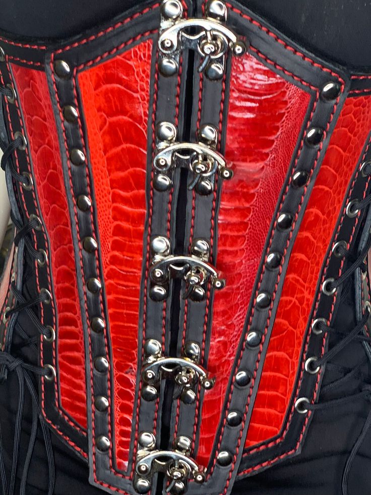 Hand made leather under bust corset in Red/Black or Turquoise/Black Colors . Corset panels feather Ostrich Leg Leather inlays for an Exotic look. This corset is designed to fit all sizes from 0 to 24. It has removable side panels to fit the small end of the size spectrum. There are five lacings to adjust to all sizes when side panels are used. 3 Lacings when the side panels are not used**. The front opens and closes easily and conveniently with five swing clasps once the corset is adjusted to your size. All Lacing is fully grommeted . All hardware is silver finish  (Swing Clasps, rivets, lacing grommets) As this is a full cowhide leather corset, there are no bonings needed. Inside is finished full grain leather and hand dyed to black The front panels are made from 3 ounce  with Ostrich Leg Steampunk Leather Corset For Cosplay, Gothic Leather Corset For Cosplay, Red Overbust Corset For Festival, Gothic Leather Corset For Party, Steampunk Red Overbust Corset, Red Gothic Overbust Corset, Gothic Leather Overbust Corset, Red Underbust Corset For Cosplay, Red Punk Fitted Corset