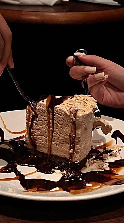 a person cutting into a piece of cake with chocolate sauce on it and caramel drizzle