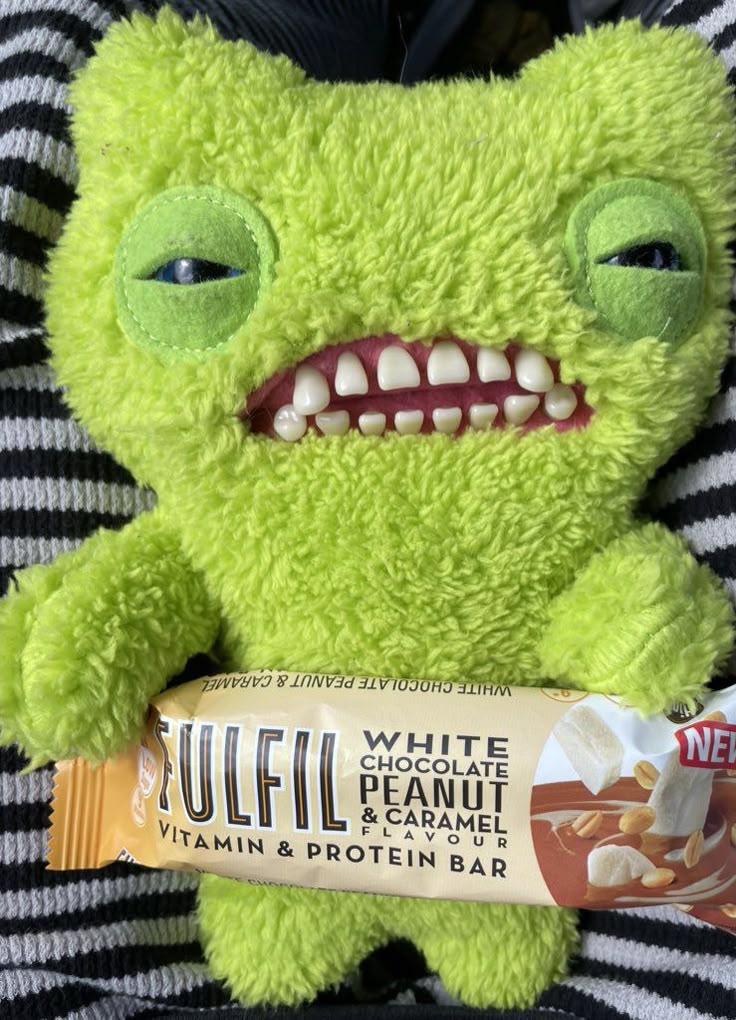 a green stuffed animal holding a bar of peanut butter