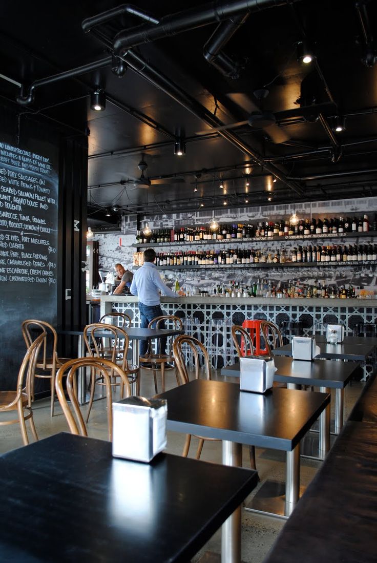 people sitting at tables in a restaurant with lots of bottles on the wall behind them