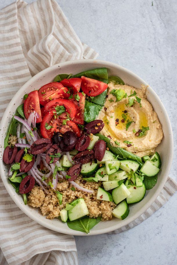 a white bowl filled with vegetables and hummus on top of a striped napkin next to a fork