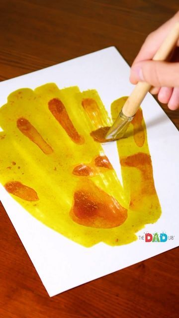 a child's hand holding a paintbrush over a piece of art