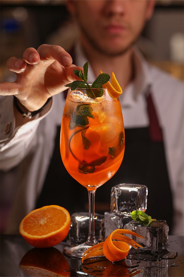 a man in an apron is holding up a glass with oranges and mint garnish