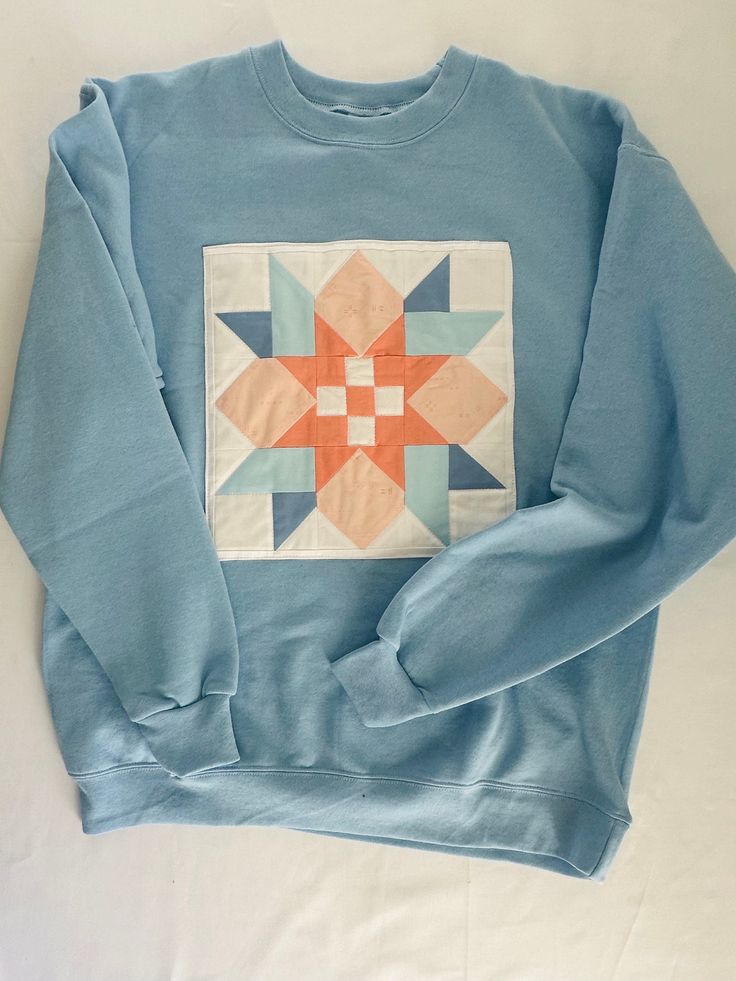 a blue sweatshirt with an orange and white patchwork design on the front, sitting on a white surface