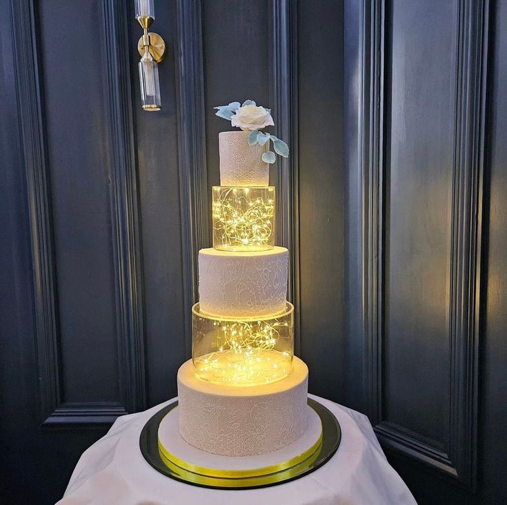 a three tiered wedding cake with lights on it