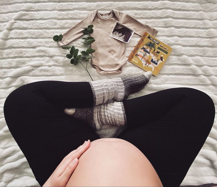 a woman laying on top of a bed next to a plant and sweater with her legs crossed