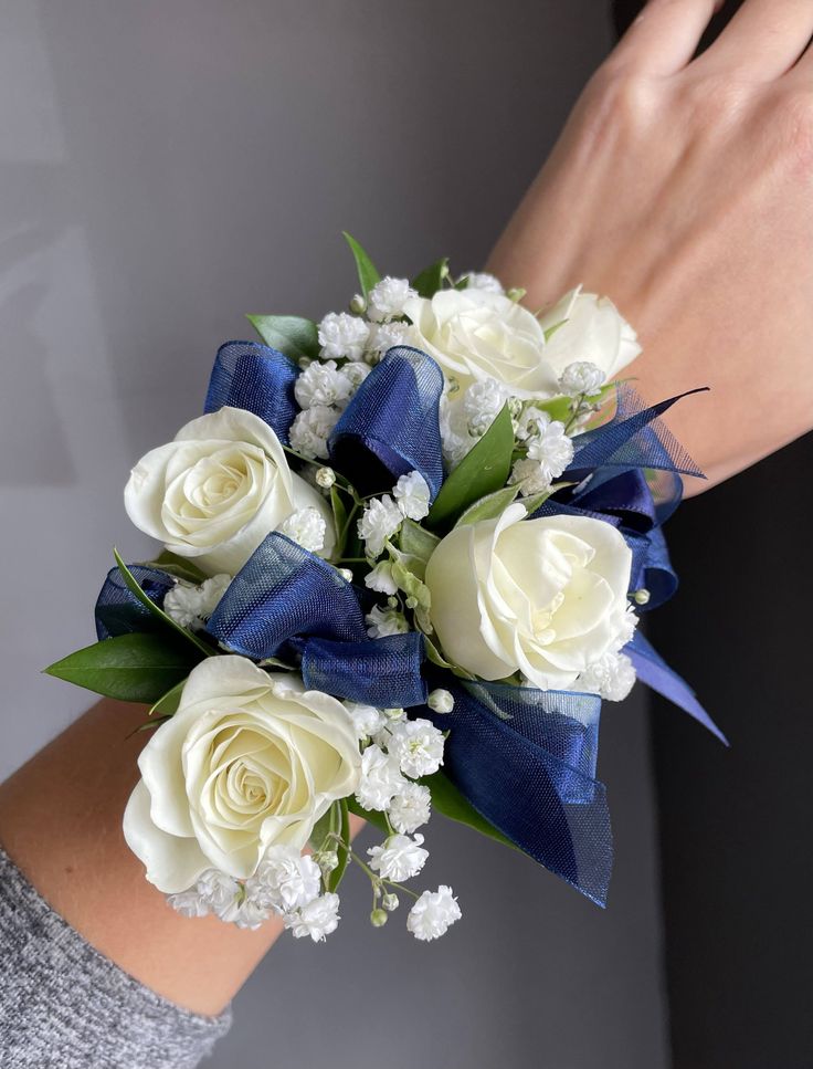 a woman's hand holding a bouquet of white roses and blue ribbon on her wrist