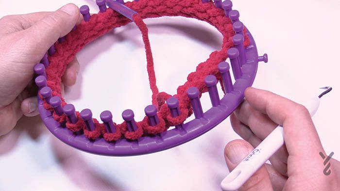 two hands are holding a purple object with red yarn on it and the other hand is using a crochet hook