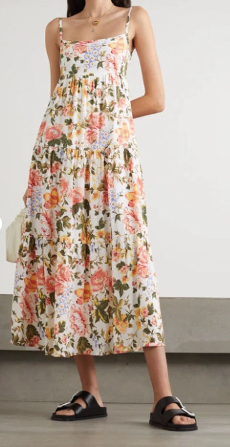 a woman wearing a dress with flowers on it and black sandals standing in front of a white wall