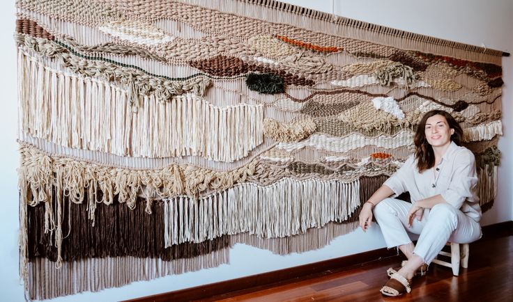 a woman sitting on a chair in front of a wall hanging with fringes and beads