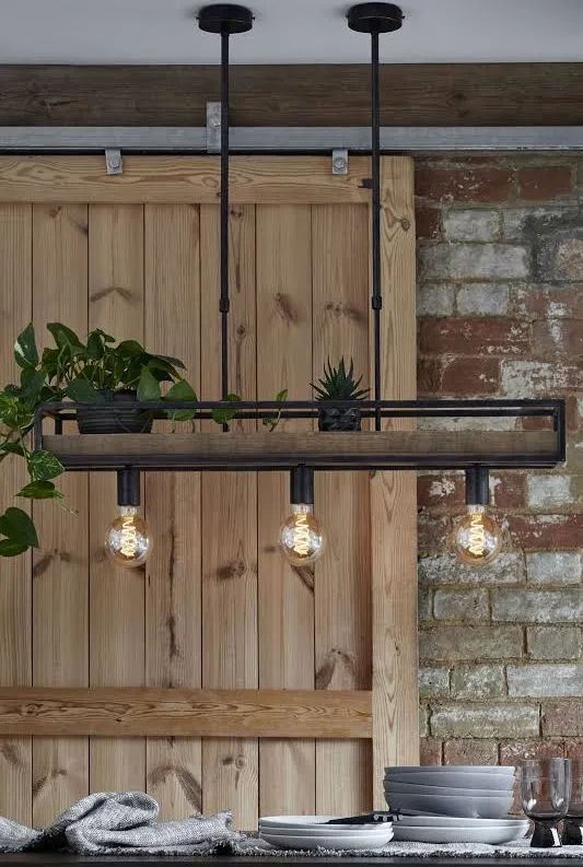 an industrial style light fixture hanging over a dining room table with potted plants on it