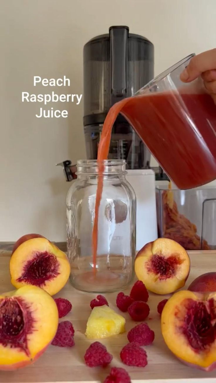 a person pouring juice into a glass next to sliced peaches and raspberries