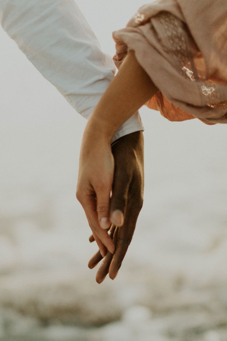 two people holding hands while walking on the beach